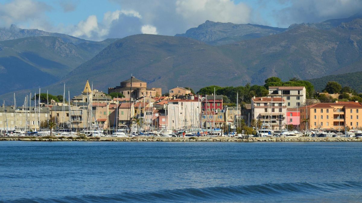 Beautiful view of the Saint-Florent harbor in Corsica, featuring colorful buildings and boats under a clear sky.